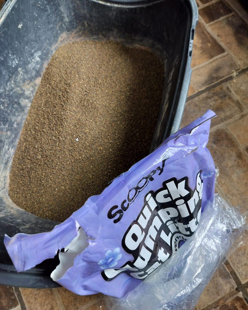 An opened purple bag of Scoopy quick clumping litter beside a grey litter box filled with fine brown litter